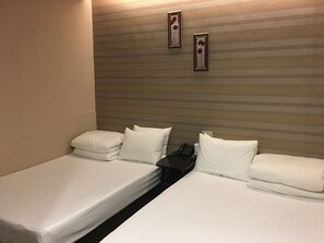 A hotel room with two single beds, each with white linens and pillows, a bedside table with a phone and a remote control, and a wall with horizontal lines and two framed pictures. - HUA CHUN LIN Hotel (New Taipei City)
