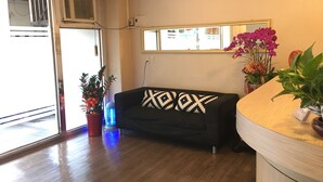 A room with a black sofa, a wooden floor, a window with a mirror, and potted plants. - HUA CHUN LIN Hotel (New Taipei City)