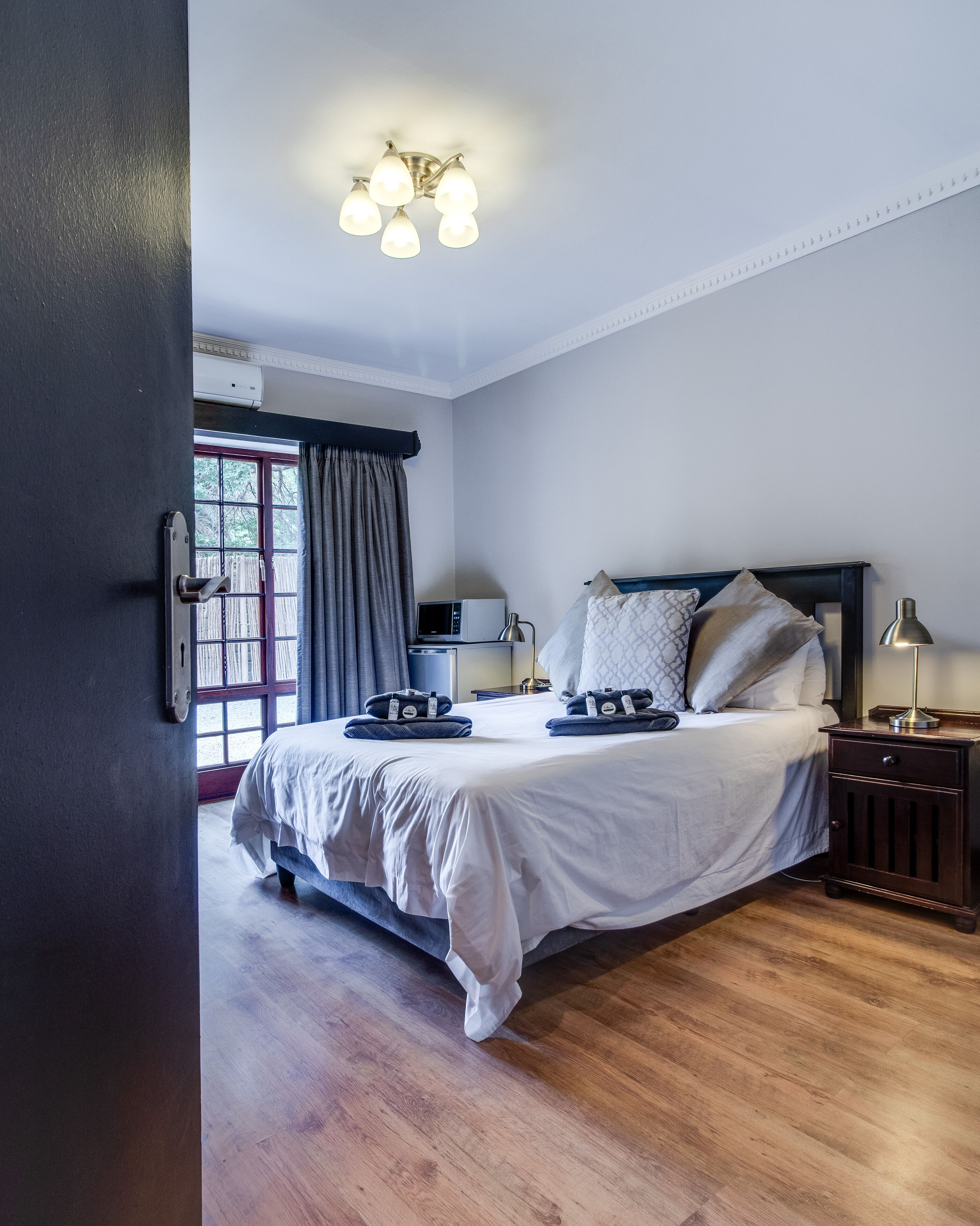 A bedroom with a bed, bedside tables, a lamp, a window with curtains, and a ceiling light fixture.