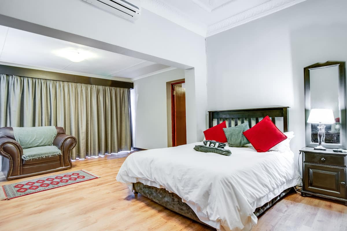 A hotel room with a large bed, a wooden floor, a sofa, a nightstand, and a mirror.