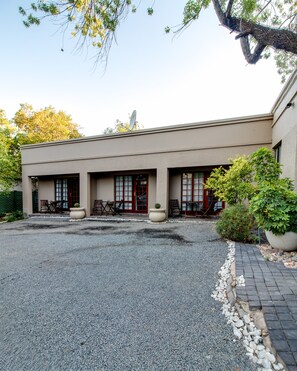A building with a gravel driveway, outdoor seating, and potted plants. - The Nightingale Guesthouse (Bloemfontein)