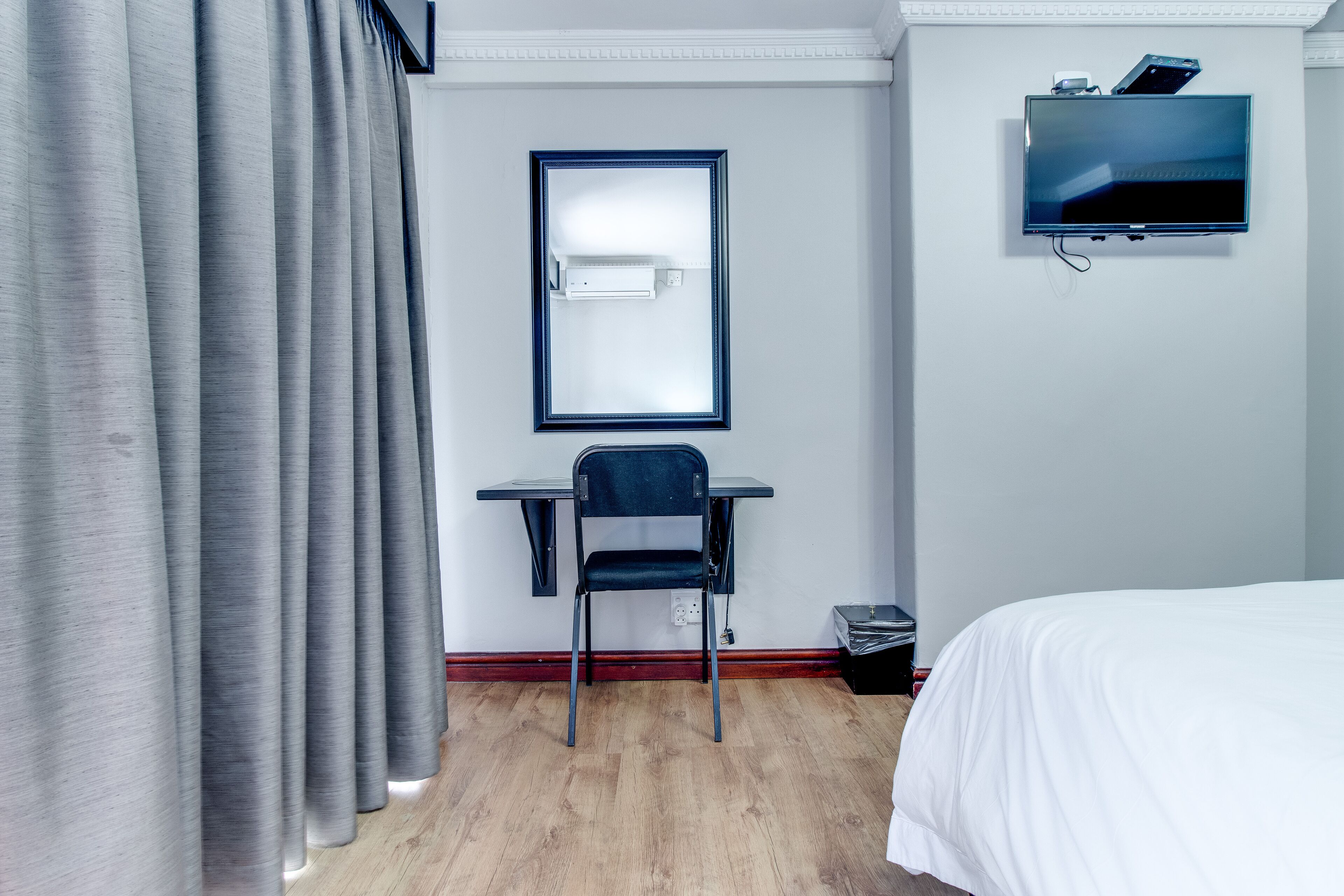 Habitación de hotel con cama, escritorio, silla, televisor y ventana con cortinas.