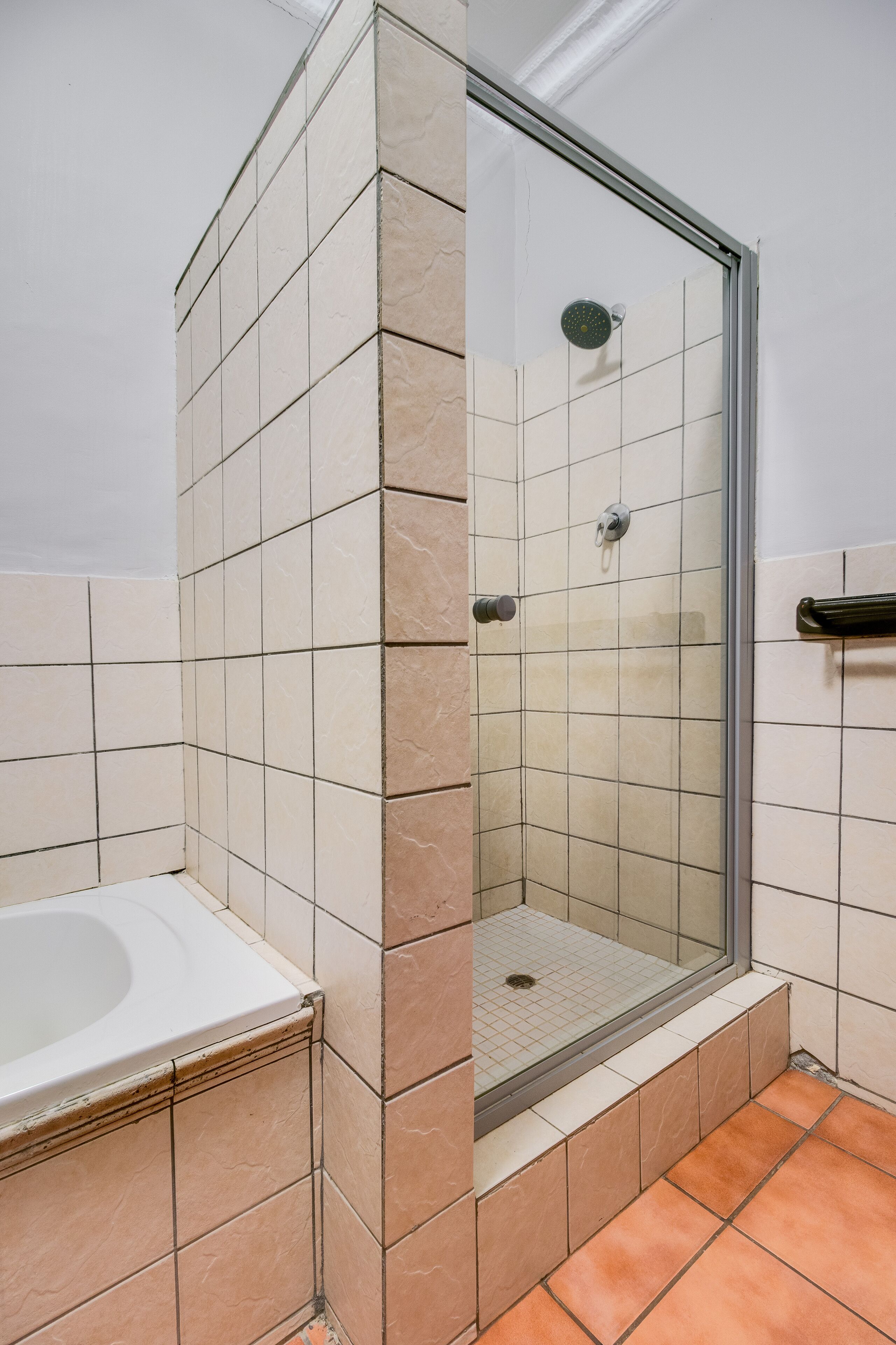 A bathroom with a glass-enclosed shower, a white bathtub, and beige tiles.