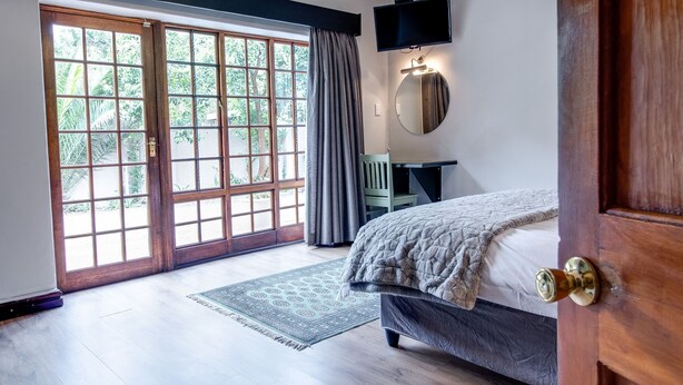 Une chambre à coucher comprenant un lit, un bureau, une chaise, un téléviseur et une grande fenêtre donnant sur un paysage verdoyant.