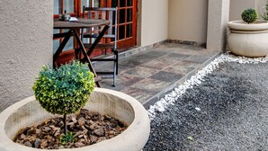 L’extérieur d’un bâtiment avec un patio, une table et des chaises en bois, ainsi que deux grands jardinières contenant de jeunes arbres.