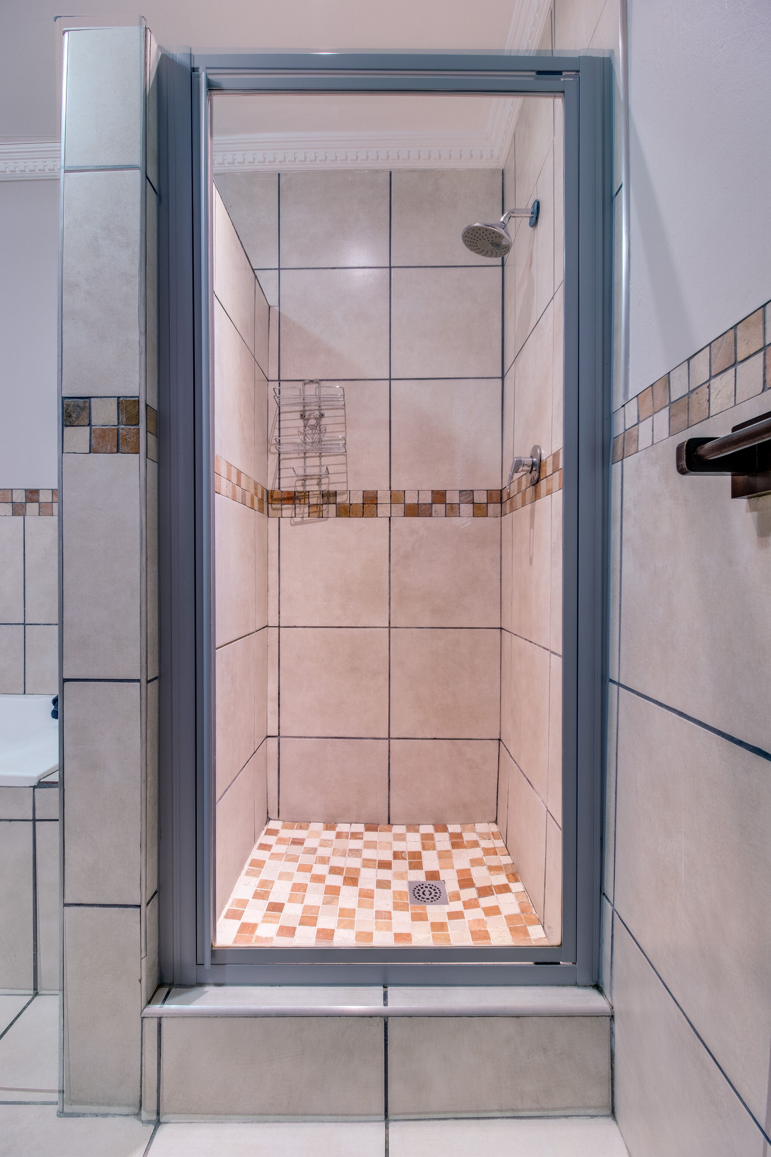A walk-in shower with a checkered floor, tiled walls, and a metal showerhead.