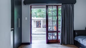 Une pièce dotée d’un plancher en bois, d’un lit, d’une porte-fenêtre coulissante donnant sur un espace extérieur avec une table et des chaises, et offrant une vue sur la verdure environnante.