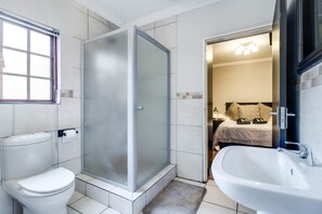 A bathroom with a toilet, a shower with frosted glass doors, and a sink. - The Nightingale Guesthouse (Bloemfontein)