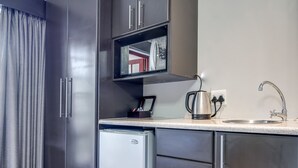 Une cuisine compacte avec des meubles de couleur sombre, un petit réfrigérateur, un four encastré, une machine à café et un évier.