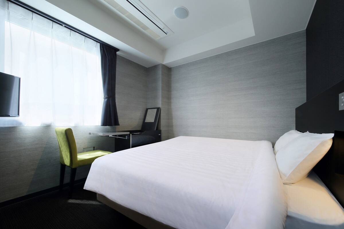 Une chambre d’hôtel avec un lit, un bureau, une chaise, une télévision et une fenêtre avec des rideaux.