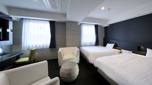 Une chambre d’hôtel avec deux lits, un bureau, une chaise et un pouf rond.