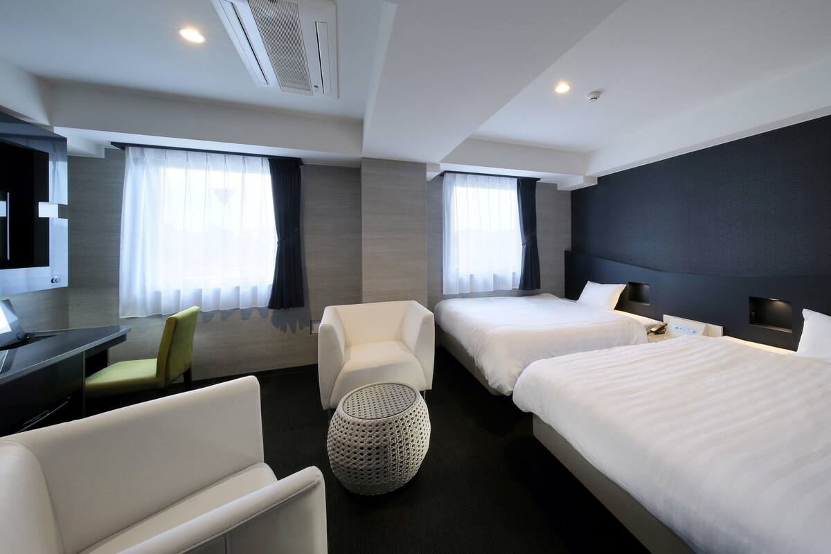 Une chambre d’hôtel avec deux lits, un bureau, une chaise et un pouf rond.