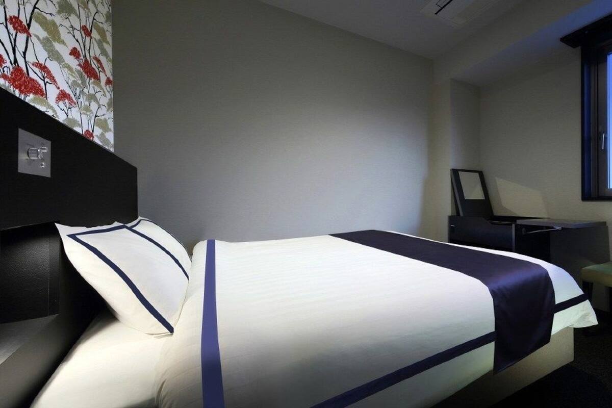 Une chambre d’hôtel avec un lit, un bureau, une chaise et une grande fenêtre.