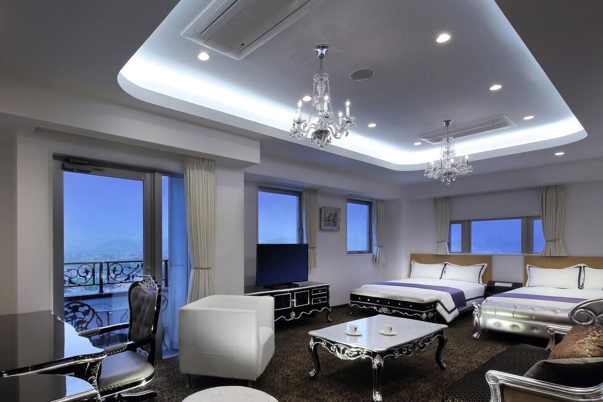 Une chambre d’hôtel avec un balcon, deux lits, une télévision, un lustre et une table à manger.