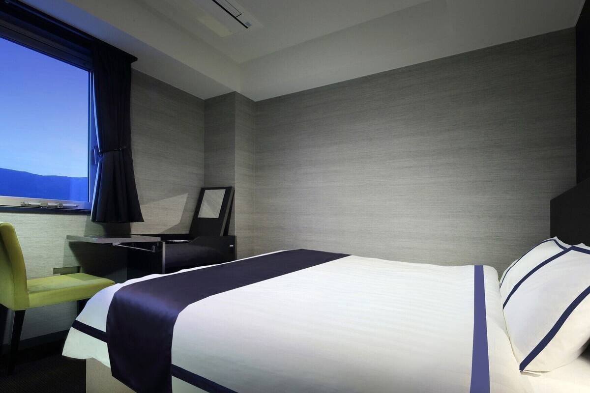 Une chambre d’hôtel avec un lit, un bureau, une chaise et une fenêtre donnant sur un paysage agréable.