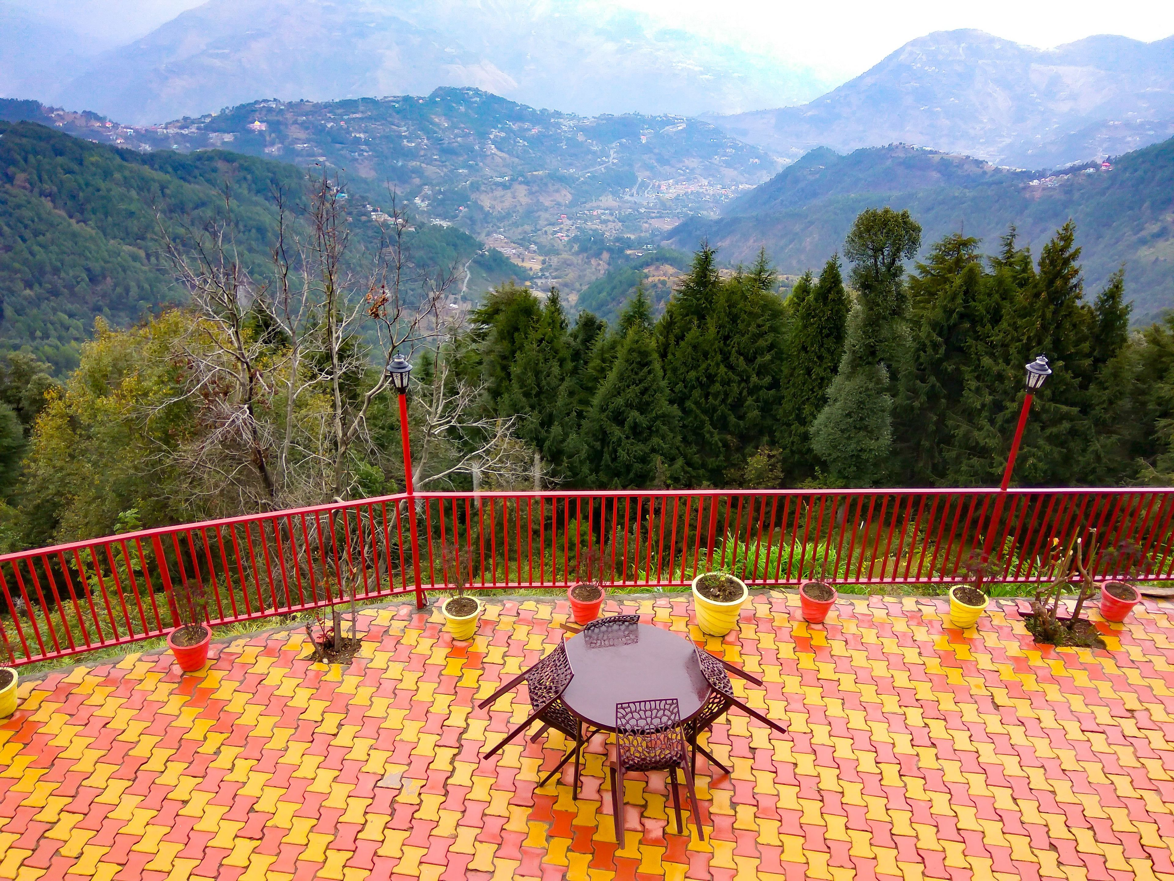 Una terraza con barandilla roja, una mesa y sillas, con vistas a un paisaje montañoso.