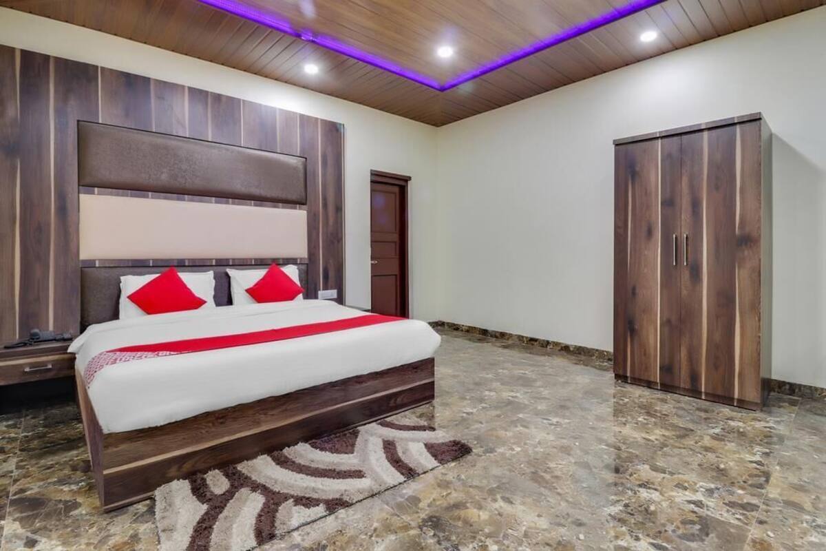 Un dormitorio con cama, cabecera de madera, un armario y una alfombra estampada.