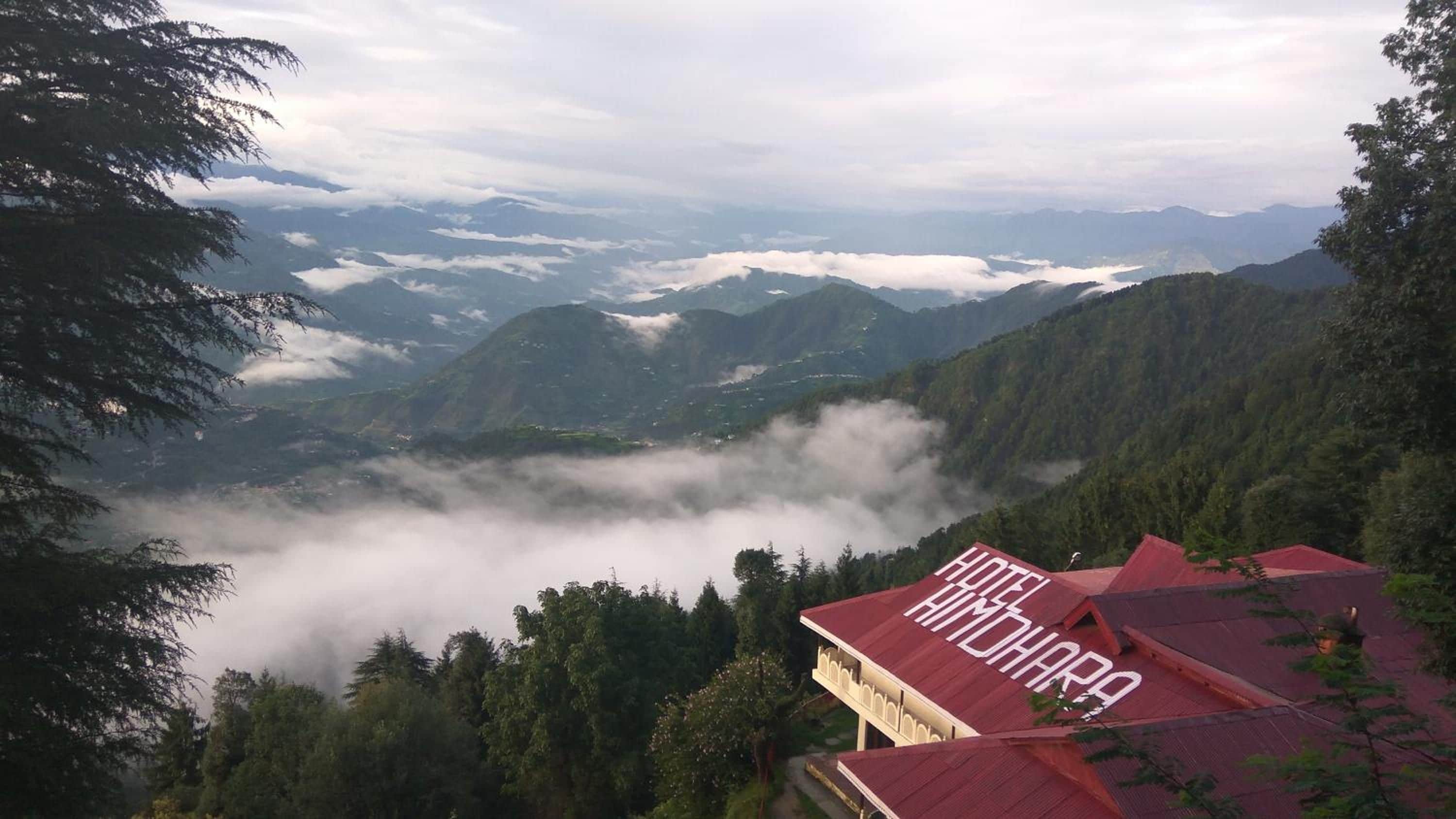 A hotel with a red roof, surrounded by forested mountains and clouds.