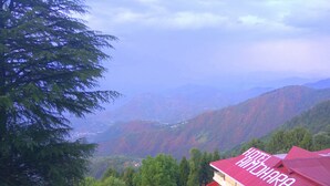 Un hotel llamado "Hotel Himalara" con techo rojo, rodeado de colinas verdes exuberantes y un telón de fondo montañoso.