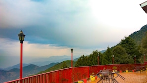 Barandal rojo con vistas a un paisaje montañoso, con un patio de baldosas y mobiliario exterior.