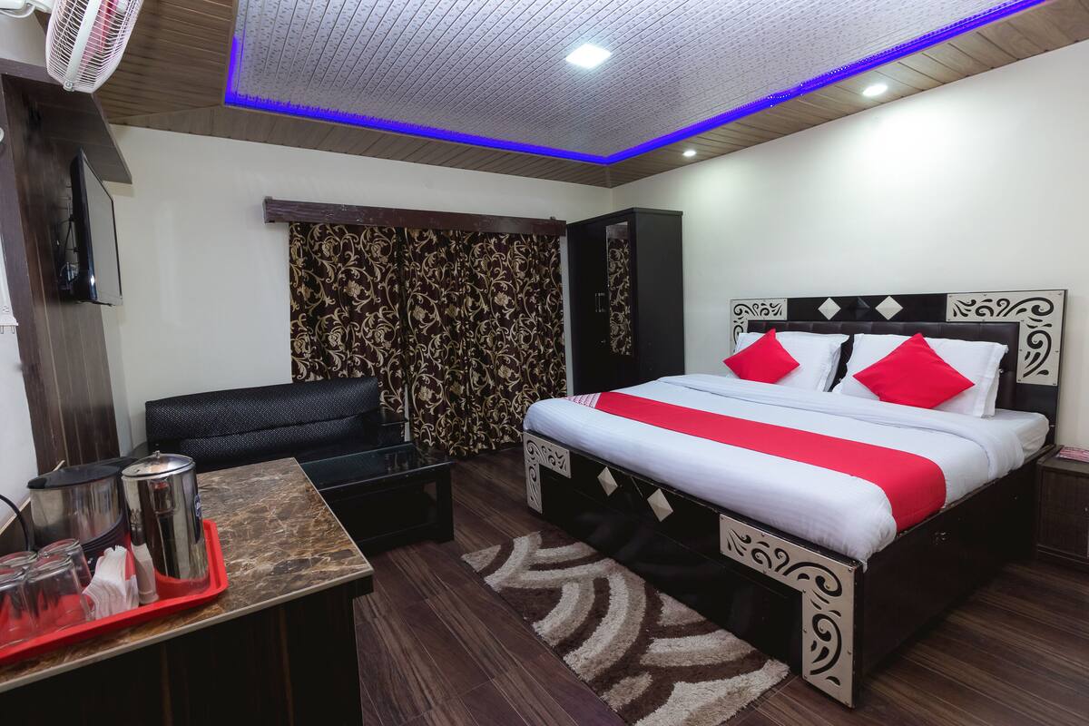 Habitación de hotel moderna con una cama grande, un sofá, una mesita con una bandeja de objetos y un panel decorativo en la pared.