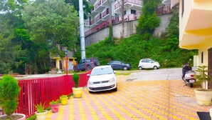 Un camino de entrada pavimentado con un coche blanco estacionado al lado, rodeado de plantas en macetas y una valla roja.