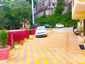 Un camino de entrada pavimentado con un coche blanco estacionado al lado, rodeado de plantas en macetas y una valla roja.