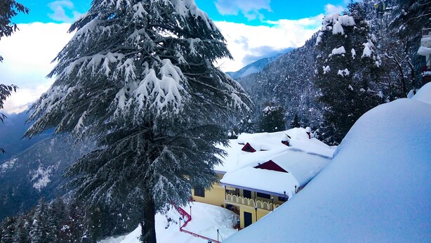 Un paisaje montañoso nevado con un edificio parcialmente oculto por árboles.