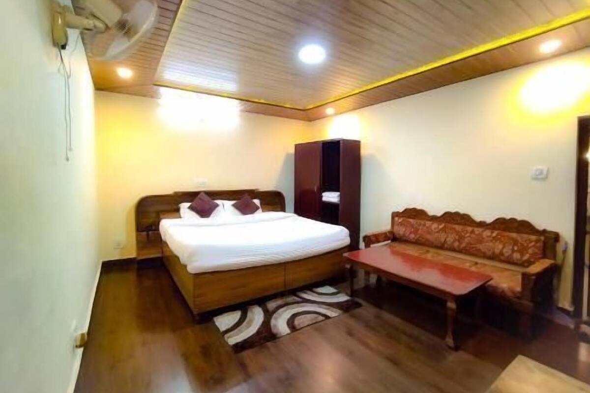 Habitación de hotel con cama de madera, sofá, una mesita y ventilador de techo.