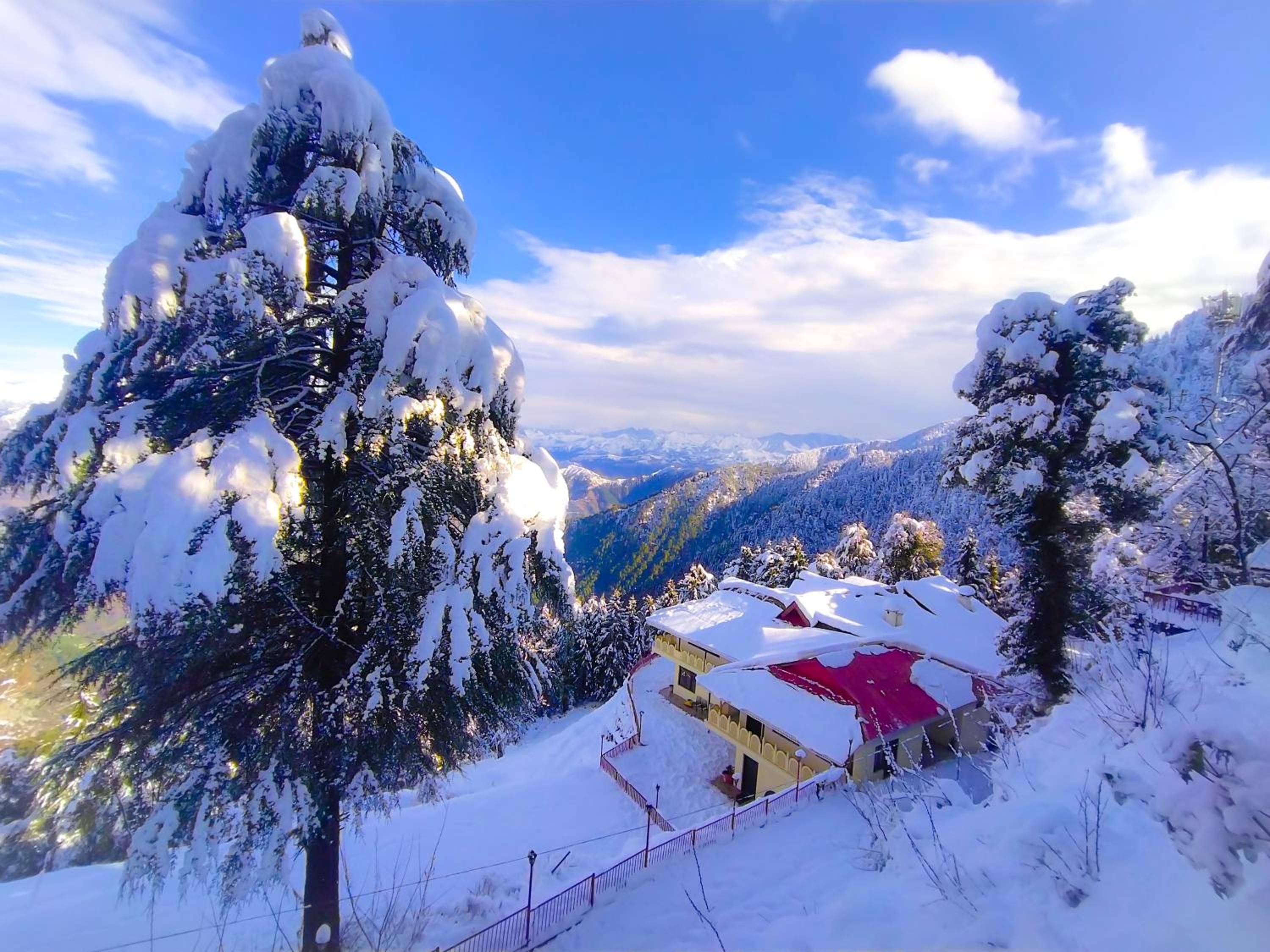 Paisagem montanhosa coberta de neve com um edifício e telhado vermelho.