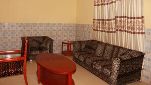 A living room with a sofa, a chair, a small table, and a patterned curtain. - Carlcon Hotel (Calabar)