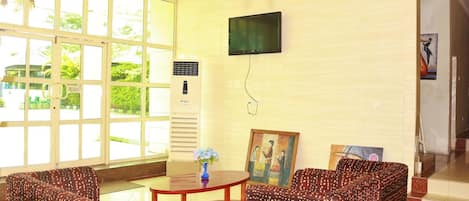 Una habitación con un ventanal grande, un televisor de pantalla plana montado en la pared, una mesita con un florero y sofás estampados.