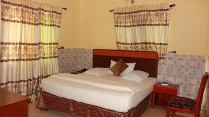 A hotel room with a large bed, two bedside tables, a chair, and curtains with a geometric pattern. - Carlcon Hotel (Calabar)