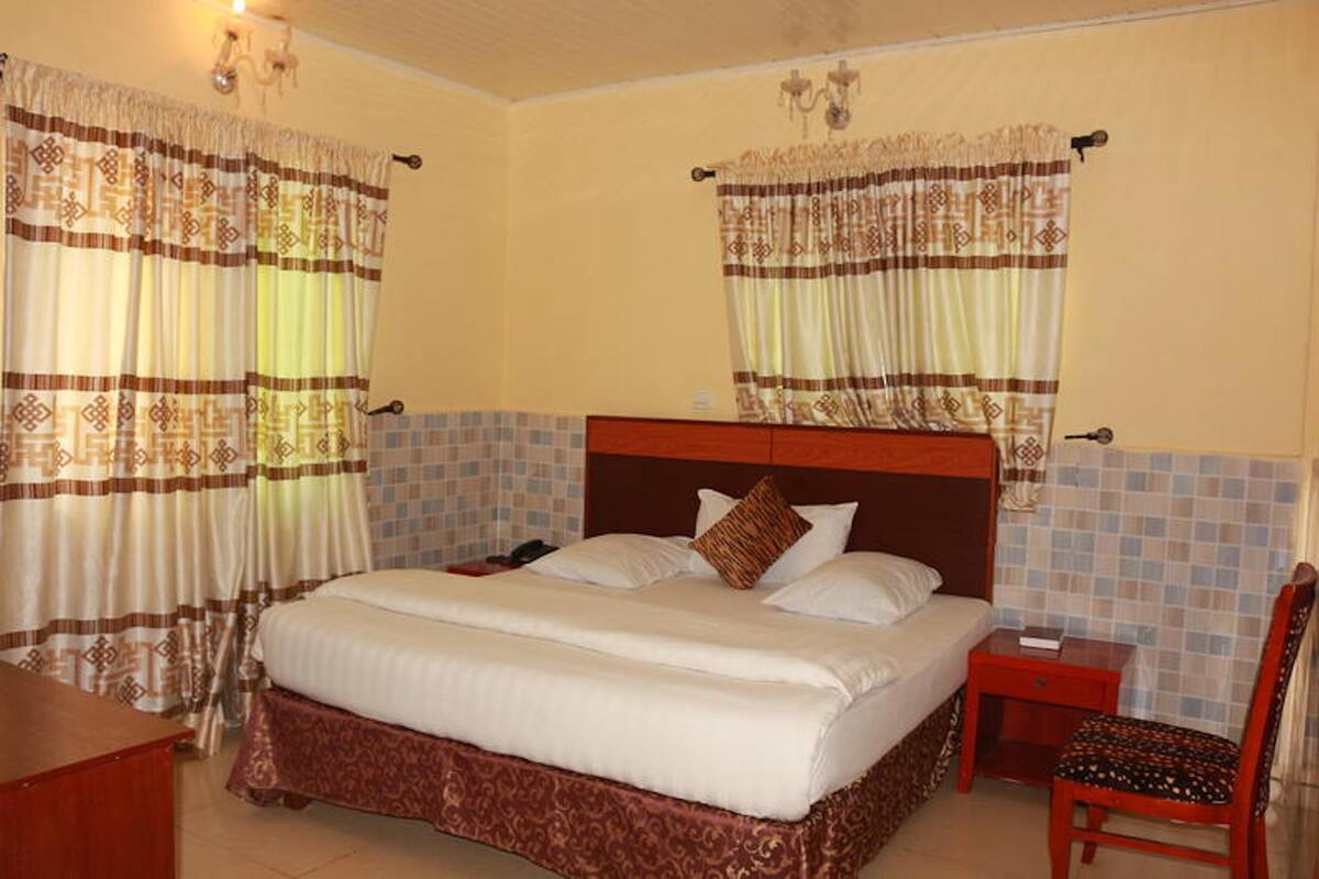 Une chambre d’hôtel avec un grand lit, deux tables de chevet, une chaise et des rideaux à motifs géométriques.
