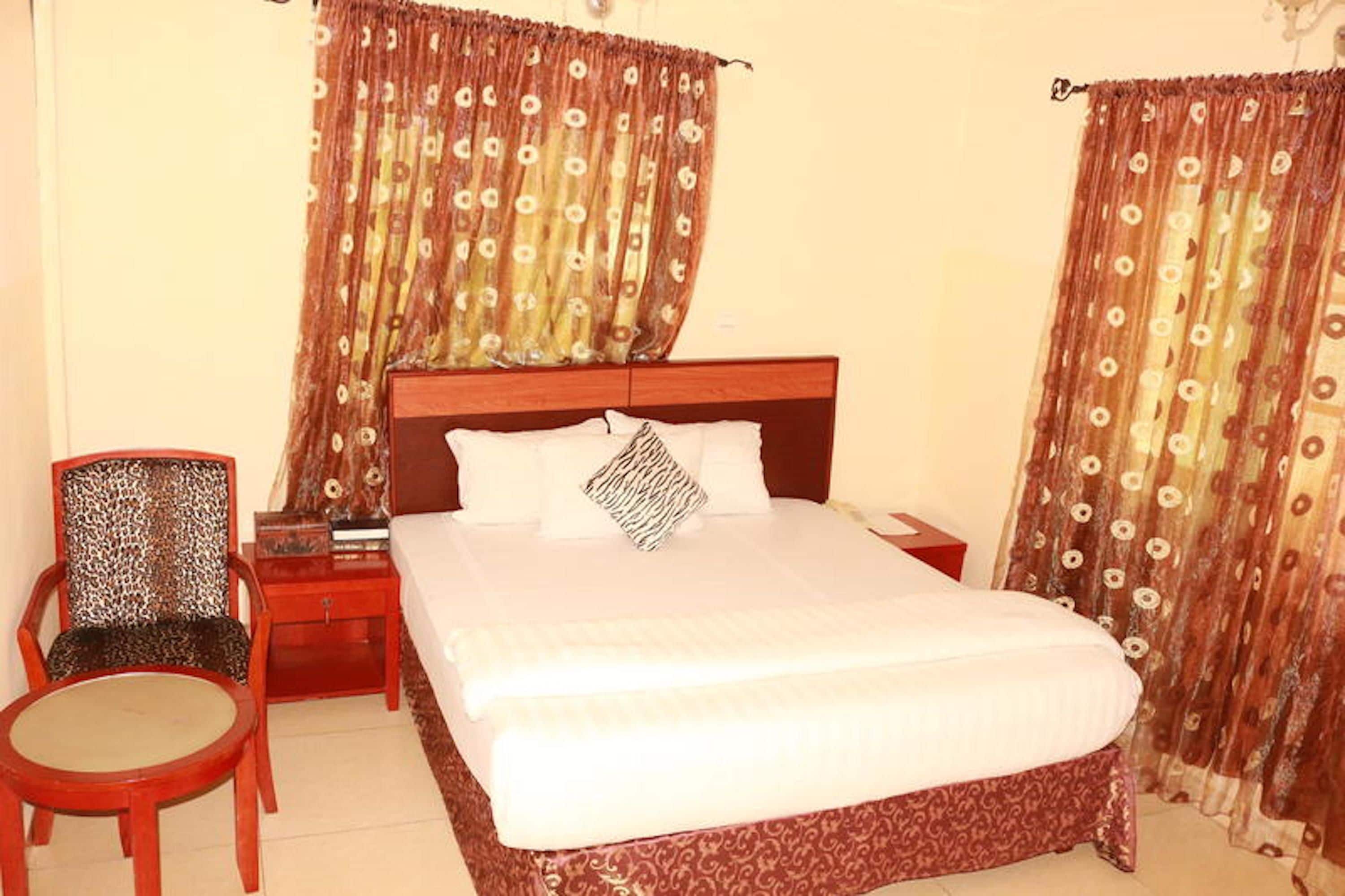 A hotel room with a bed, a chair, a nightstand, and curtains.