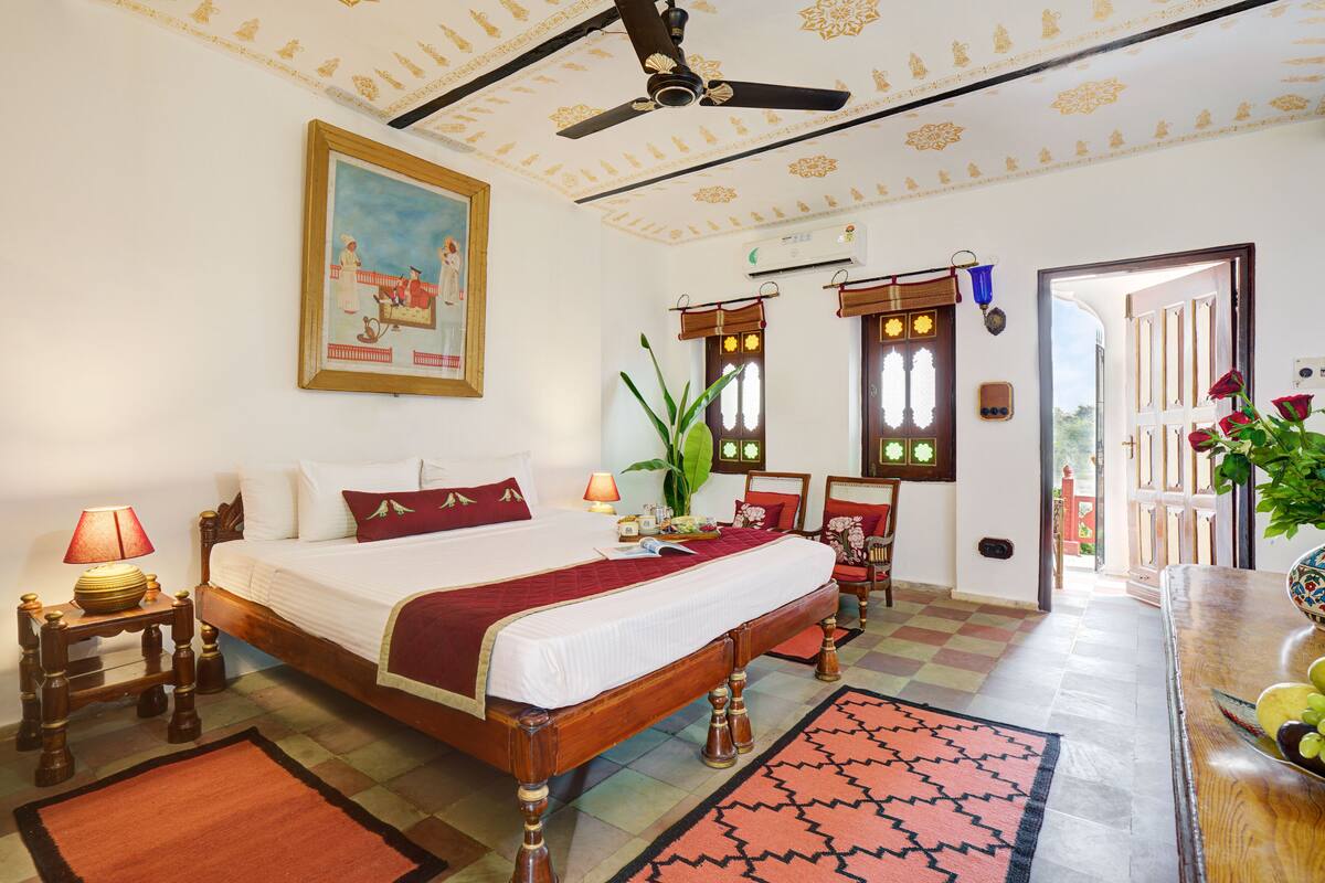 A well-appointed bedroom with a large bed, a ceiling fan, a painting, and a view of the outside.