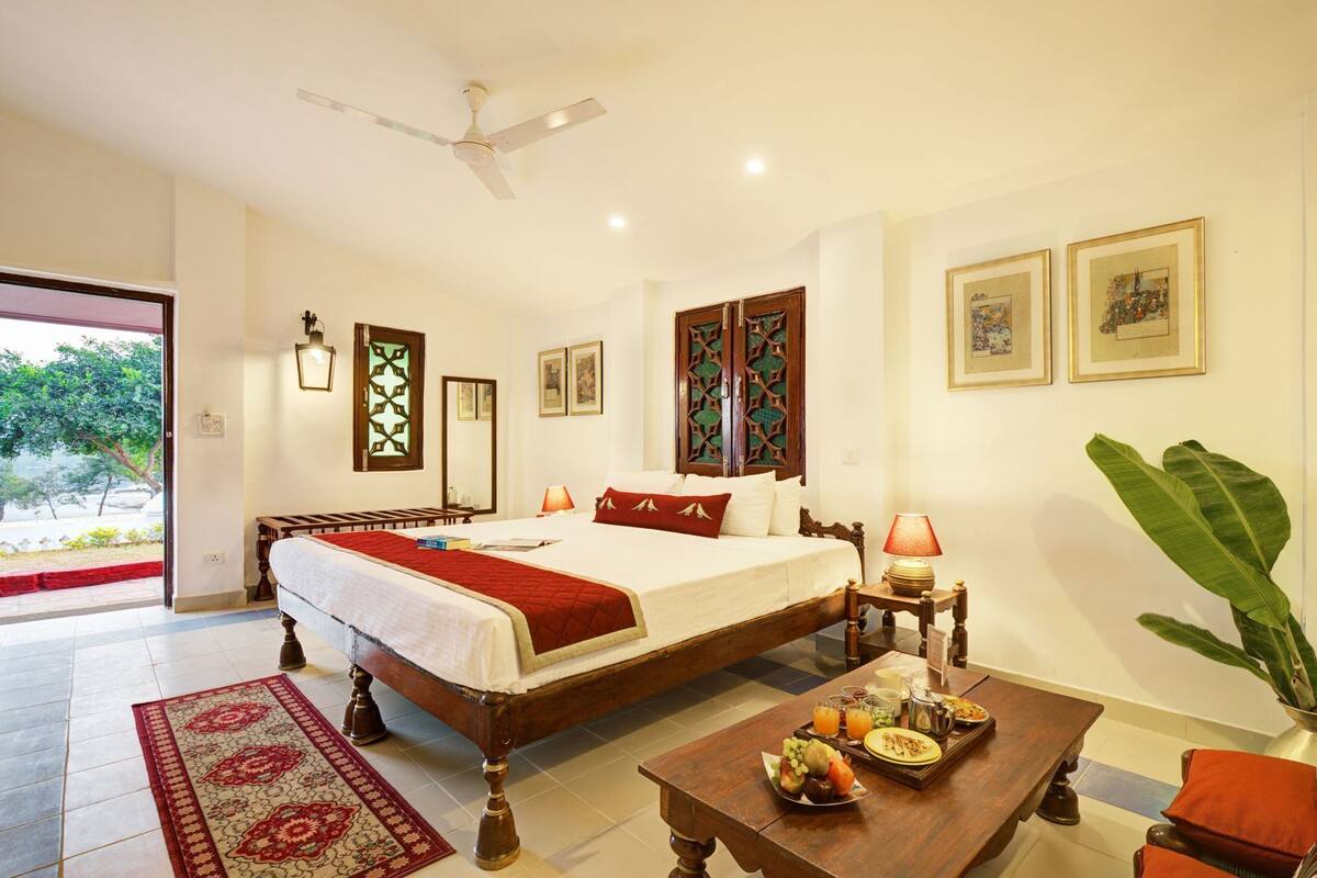 A hotel room with a bed, bedside table, lamp, and a dining table with breakfast items.