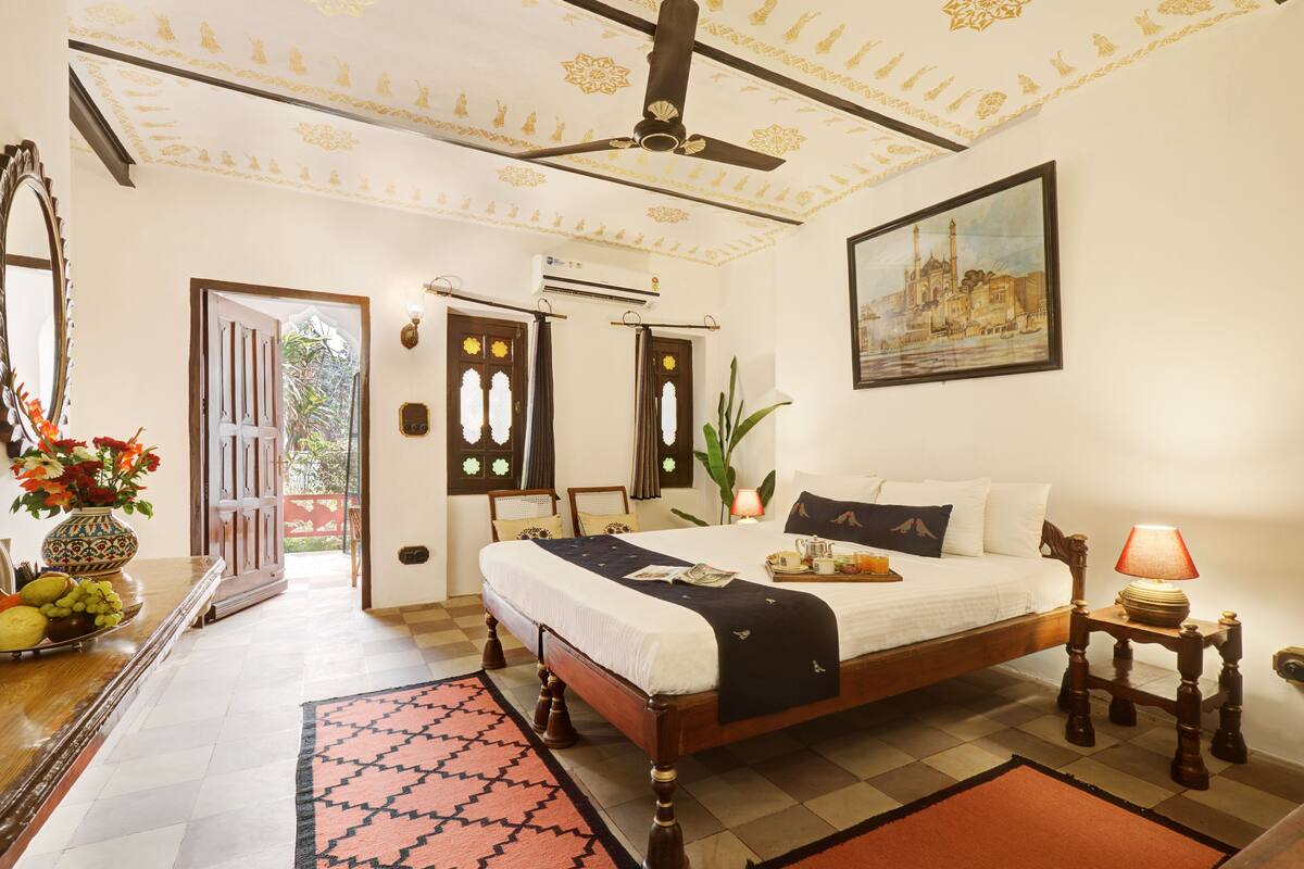 A bedroom with a bed, a ceiling fan, a painting, a lamp, and a window with curtains.