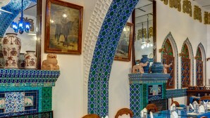 Un coin repas avec des murs recouverts de carreaux bleus, des chaises en bois et une table en verre dressée pour le repas.