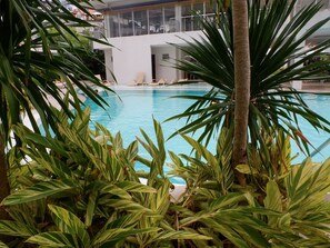 A swimming pool surrounded by lush green plants, with a modern building in the background. - Studio 610 (Cebu City)