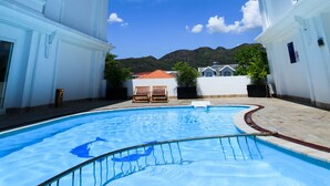 A swimming pool surrounded by white buildings with balconies, under a clear blue sky. - Paragon Villa Hotel (Nam Nha Trang)
