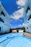 Una piscina rodeada de edificios blancos con balcones, bajo un cielo azul despejado.