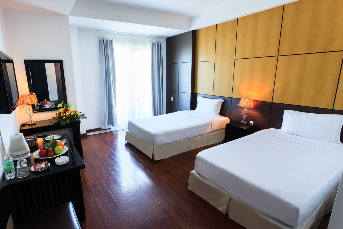 A hotel room with two beds, a desk with a lamp, a mirror, and a window with curtains.