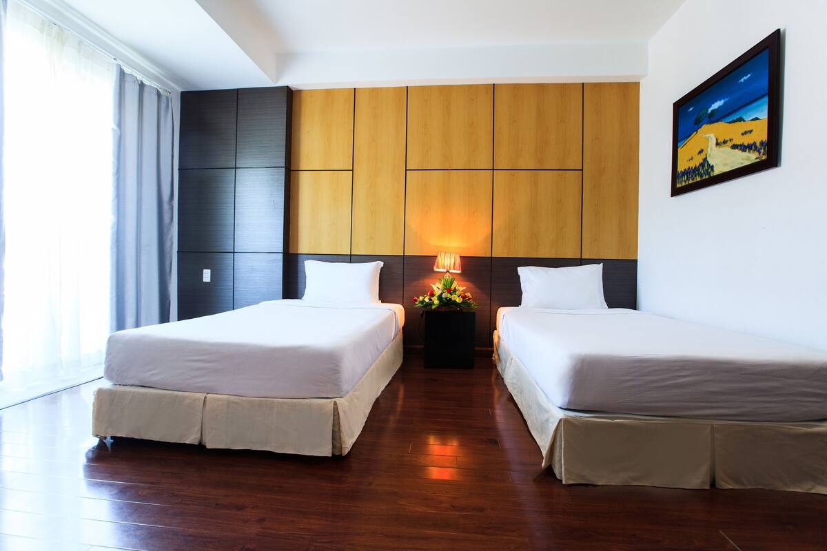A hotel room with two beds, a wooden headboard, a nightstand with a lamp, and a painting on the wall.