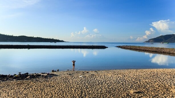 A beach with calm waters, a rocky shoreline, and a person standing in the water. - Paragon Villa Hotel (Nam Nha Trang)