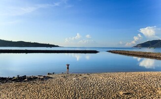Una playa con aguas tranquilas, una costa rocosa y una persona de pie en el agua.