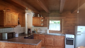A wooden cabin-style kitchen with a central island, built-in cabinets, a stove, and a refrigerator. - Appartementhaus Gugganig (Flattach)