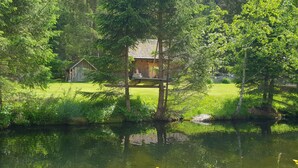 A rustic cabin with a wooden deck and a pond in front. - Appartementhaus Gugganig (Flattach)