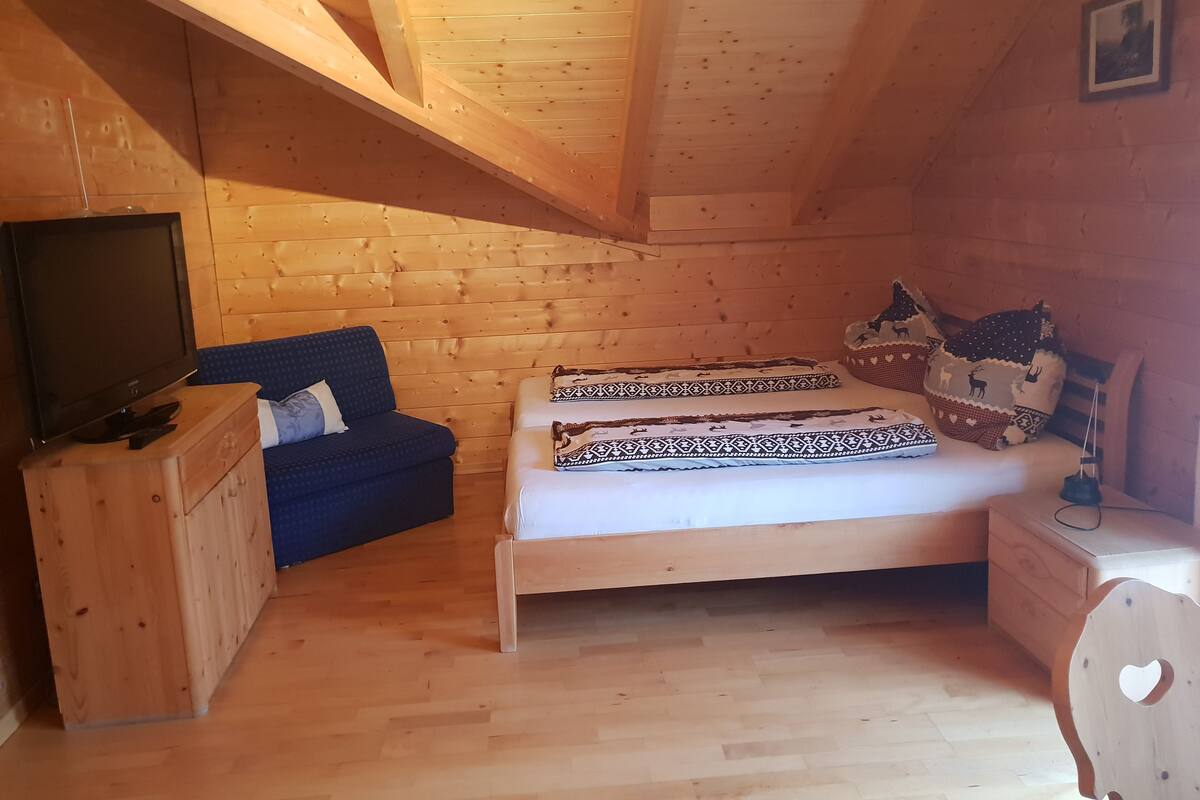 A cozy wooden room with a bed, a blue sofa, and a TV on a wooden cabinet.