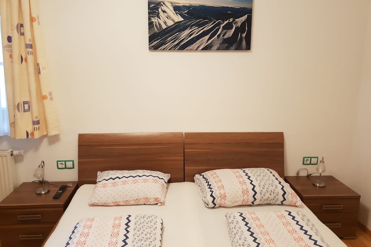 A double bed with patterned bedding, a wooden headboard, and a nightstand with a lamp and remote control.